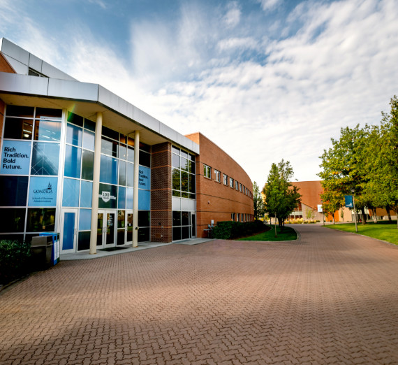 GU bulldog head logo and Pac-12 logo side-by-side over a photo of the Gonzaga University campus at sunset.